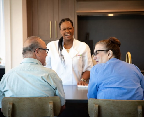 Personal chef laughing with an elderly couple in their kitchen.