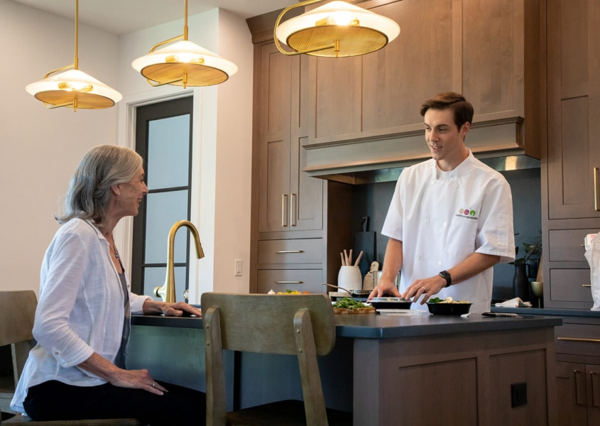 Personal chef chatting with elderly woman eating.
